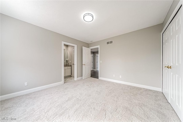 unfurnished bedroom featuring light carpet, ensuite bathroom, and a closet