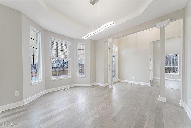 unfurnished room with a tray ceiling, ornate columns, and light hardwood / wood-style floors