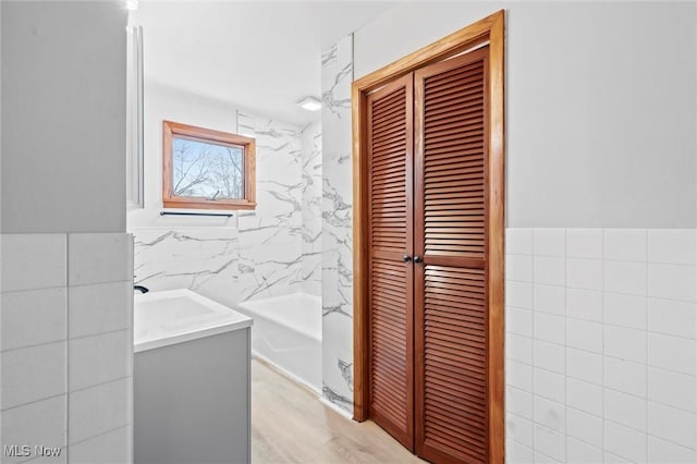 bathroom featuring hardwood / wood-style floors, vanity, a tub to relax in, and tile walls