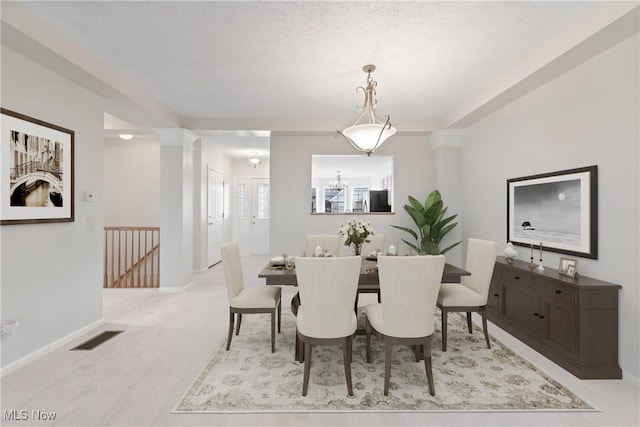 dining room with light carpet, a textured ceiling, and ornate columns