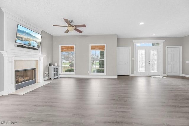 unfurnished living room with ceiling fan, french doors, wood-type flooring, a textured ceiling, and a fireplace