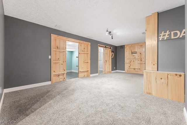 carpeted spare room featuring a barn door, rail lighting, and a textured ceiling