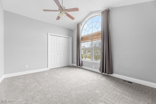 unfurnished bedroom with ceiling fan, a closet, carpet floors, and vaulted ceiling