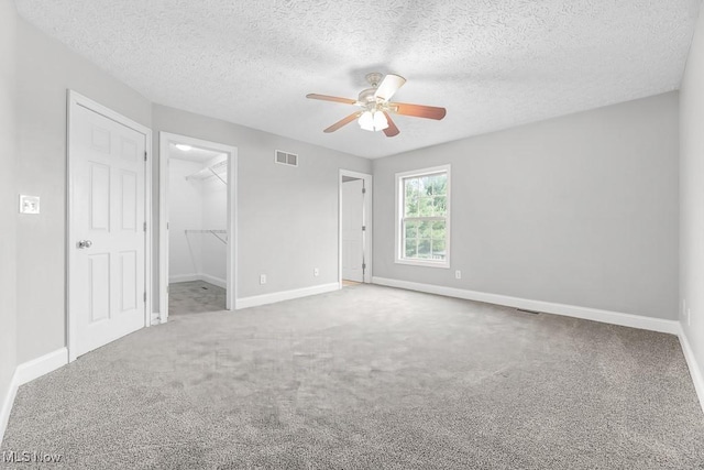 unfurnished bedroom with a walk in closet, carpet flooring, ceiling fan, a textured ceiling, and a closet