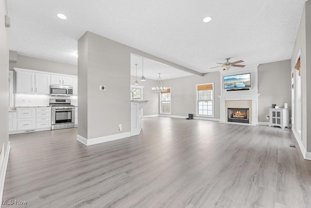 unfurnished living room featuring a tile fireplace, light hardwood / wood-style flooring, ceiling fan, a textured ceiling, and beamed ceiling