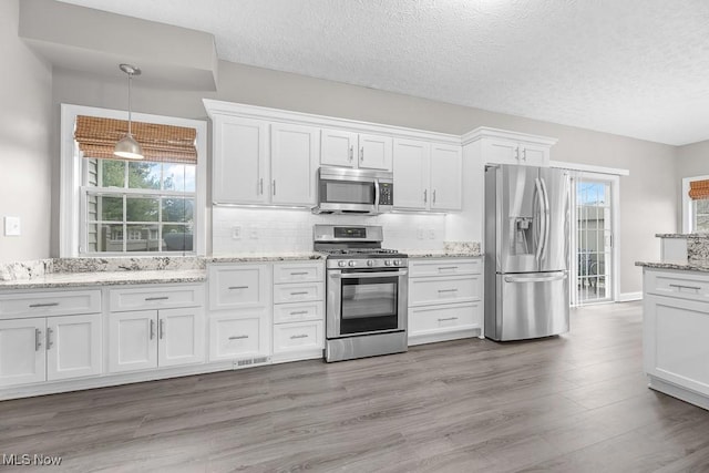 kitchen with decorative backsplash, white cabinetry, hanging light fixtures, and appliances with stainless steel finishes