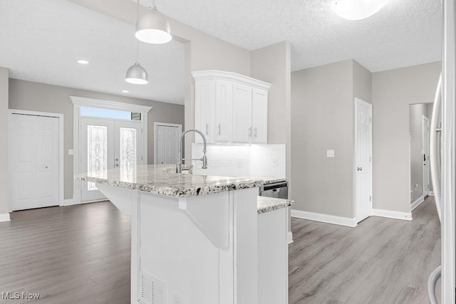 kitchen featuring white cabinets, hanging light fixtures, light wood-type flooring, light stone countertops, and a textured ceiling