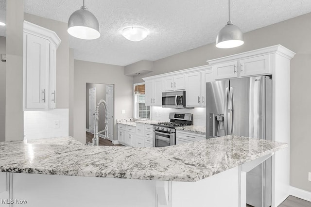 kitchen featuring pendant lighting, white cabinets, sink, appliances with stainless steel finishes, and kitchen peninsula