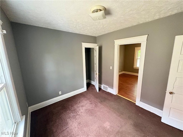 unfurnished bedroom featuring dark colored carpet and a textured ceiling