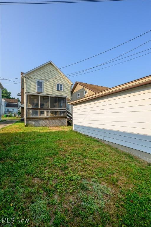 rear view of house featuring a lawn and a sunroom