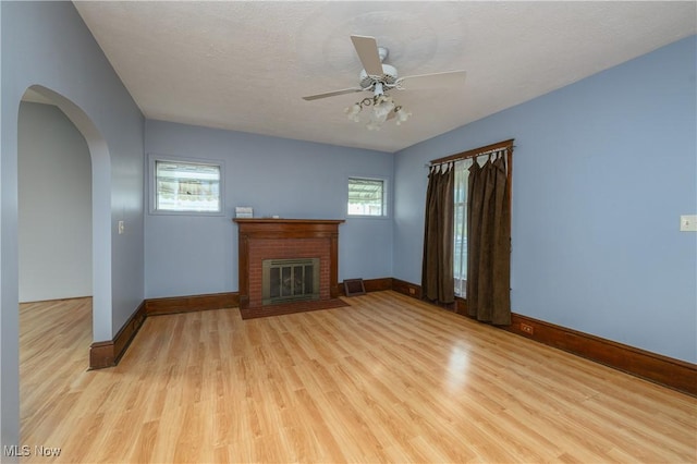 unfurnished living room with ceiling fan, light hardwood / wood-style floors, a textured ceiling, and a brick fireplace