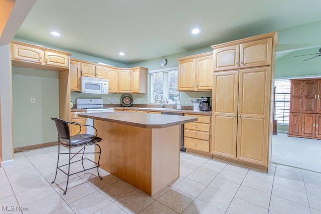 kitchen featuring white appliances, light tile patterned floors, light brown cabinetry, a kitchen island, and a breakfast bar area