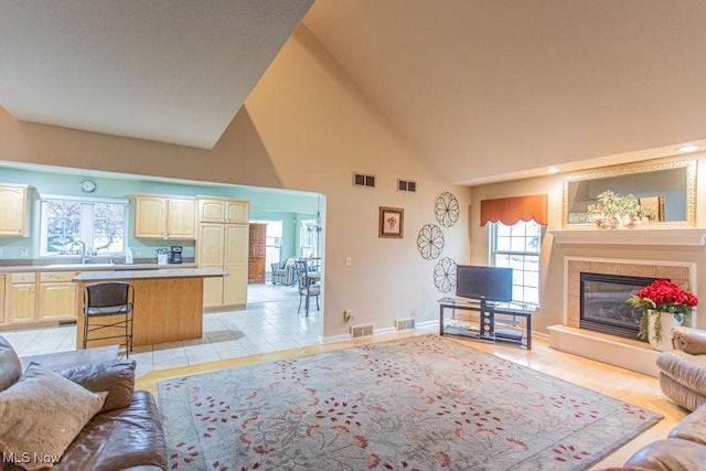 tiled living room with sink, high vaulted ceiling, and a tiled fireplace