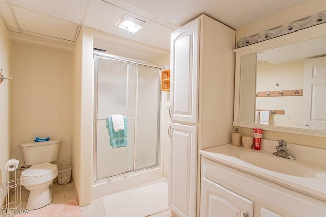 bathroom featuring a paneled ceiling, vanity, toilet, and a shower with door