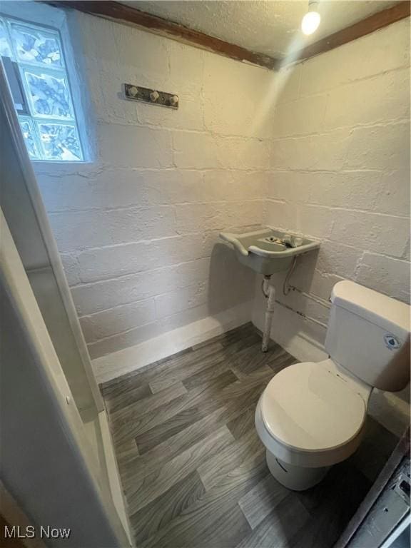 bathroom with wood-type flooring, brick wall, and toilet