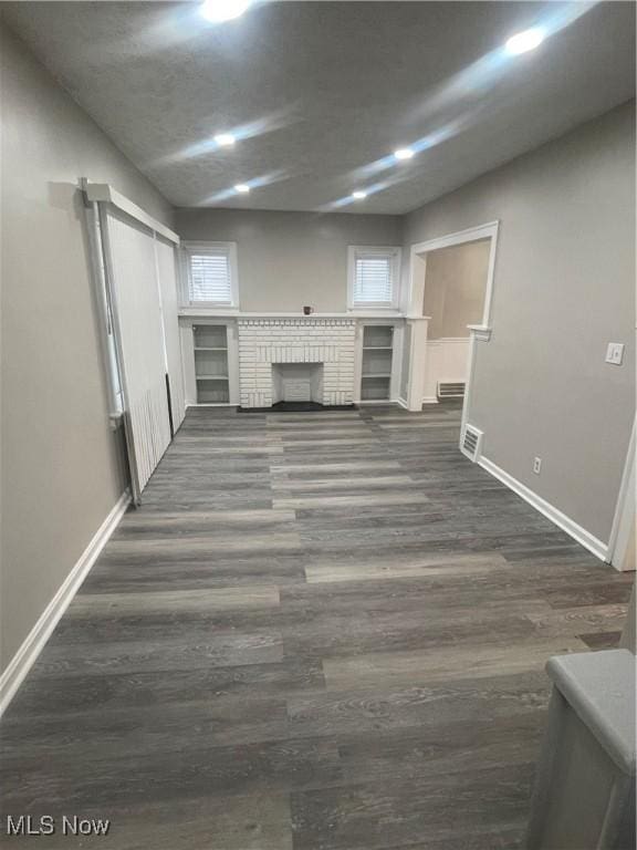 unfurnished living room with a wealth of natural light, dark hardwood / wood-style flooring, and a brick fireplace