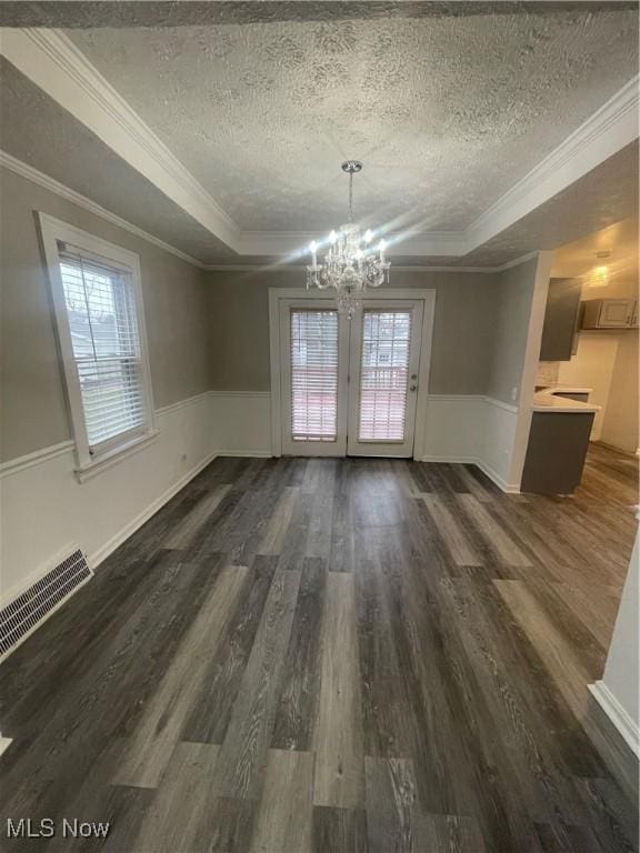 unfurnished dining area with ornamental molding, a textured ceiling, a raised ceiling, a notable chandelier, and dark hardwood / wood-style floors