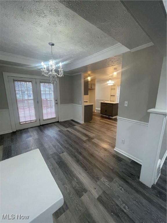 unfurnished dining area featuring a textured ceiling, a notable chandelier, crown molding, and dark wood-type flooring