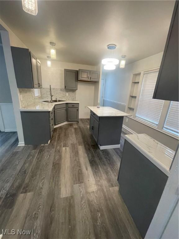 kitchen with sink, decorative backsplash, gray cabinets, a kitchen island, and dark hardwood / wood-style flooring