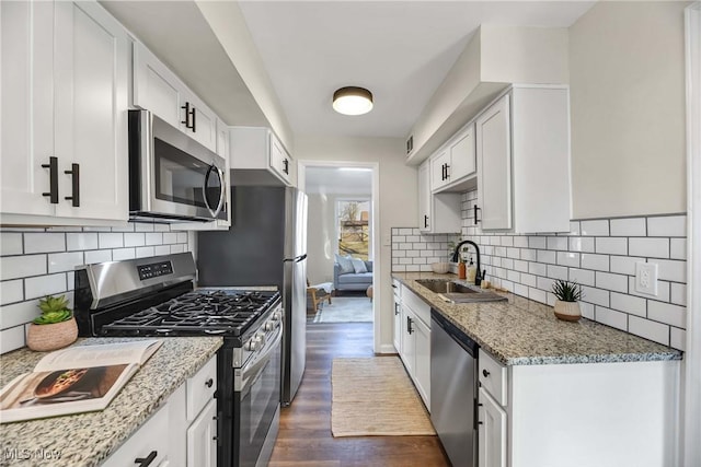 kitchen with white cabinets, stainless steel appliances, light stone counters, and sink