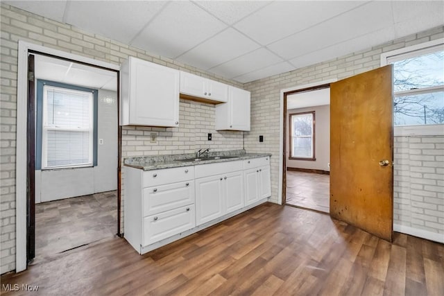 kitchen with white cabinetry, a drop ceiling, light stone countertops, sink, and brick wall