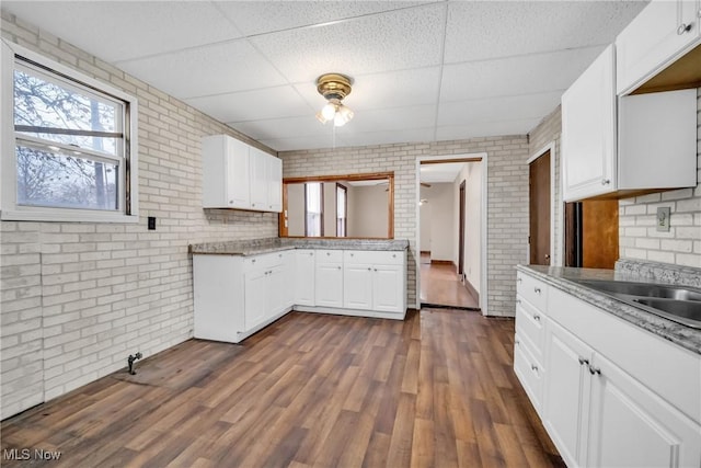 kitchen featuring a paneled ceiling, sink, dark hardwood / wood-style floors, white cabinetry, and brick wall