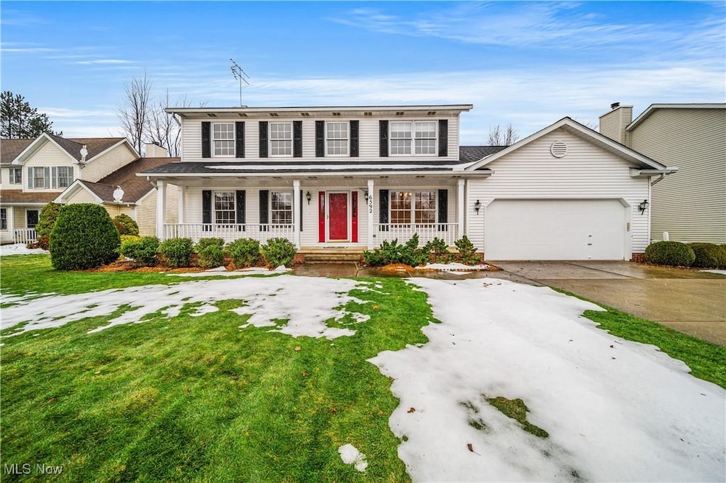 view of front of property featuring covered porch, a garage, and a front lawn