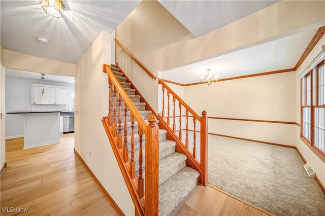 stairway with a textured ceiling, ornamental molding, a notable chandelier, and hardwood / wood-style flooring