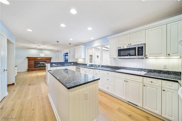 kitchen with light wood-type flooring, stainless steel appliances, a brick fireplace, and hanging light fixtures