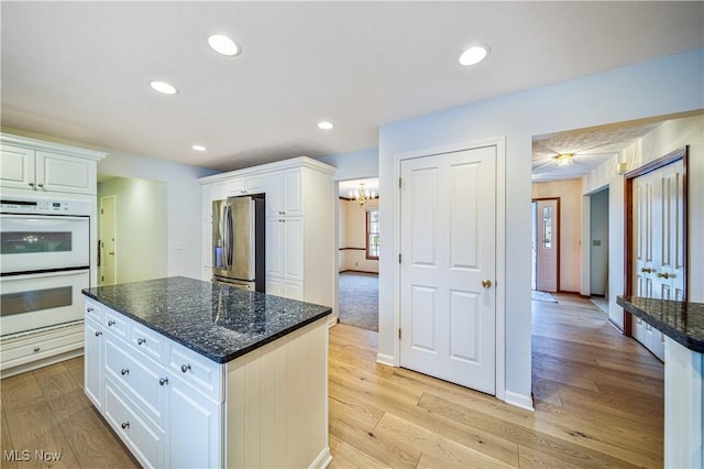 kitchen with stainless steel fridge with ice dispenser, white cabinetry, double oven, and dark stone countertops