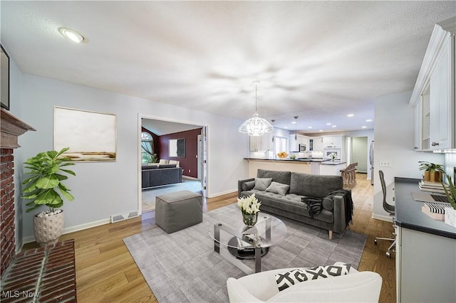 living room with light hardwood / wood-style floors, a notable chandelier, and a brick fireplace