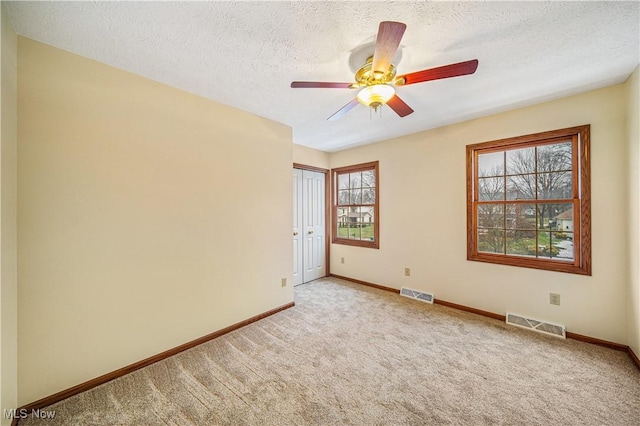 spare room featuring ceiling fan, light colored carpet, and a textured ceiling