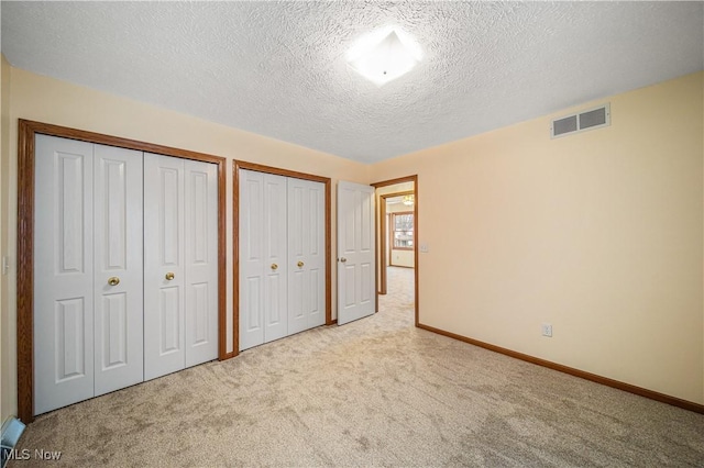 unfurnished bedroom featuring multiple closets, light carpet, and a textured ceiling