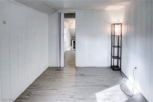 empty room featuring wood walls, light hardwood / wood-style floors, and lofted ceiling