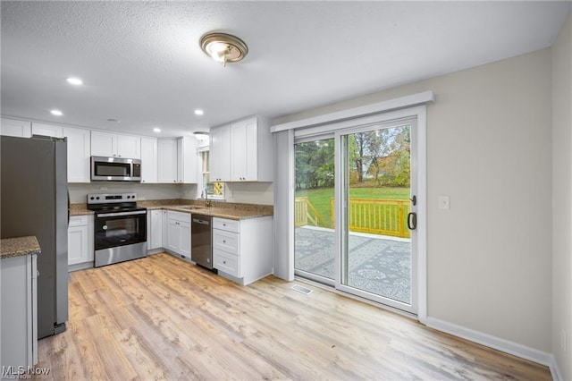 kitchen with light stone countertops, appliances with stainless steel finishes, white cabinetry, and sink