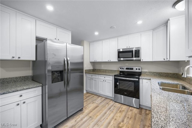 kitchen with light stone countertops, appliances with stainless steel finishes, sink, light hardwood / wood-style floors, and white cabinetry