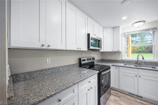 kitchen with light stone countertops, appliances with stainless steel finishes, light wood-type flooring, sink, and white cabinetry