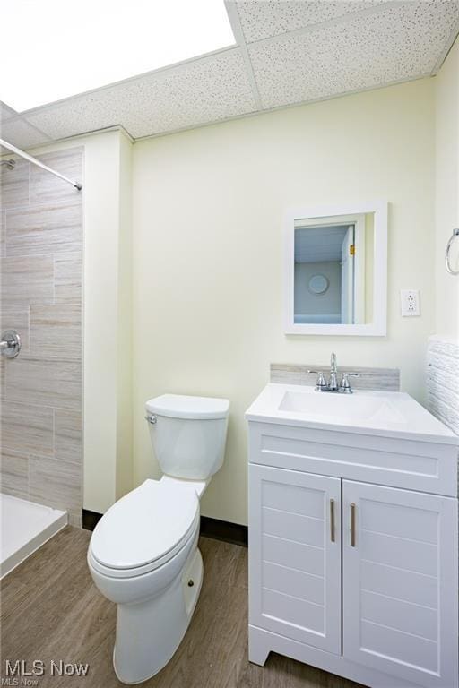 bathroom with tiled shower, vanity, toilet, and a drop ceiling