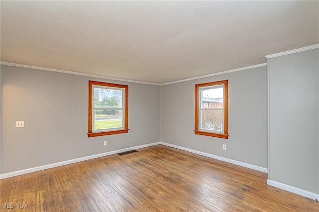 empty room with a wealth of natural light, crown molding, and wood-type flooring