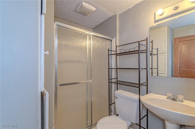 bathroom featuring sink, a shower with door, a textured ceiling, and toilet