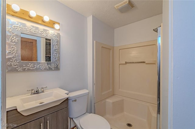 bathroom with a textured ceiling, vanity, toilet, and a shower