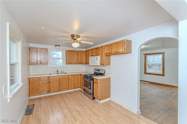 kitchen with ceiling fan, sink, stainless steel gas range, tasteful backsplash, and light hardwood / wood-style floors