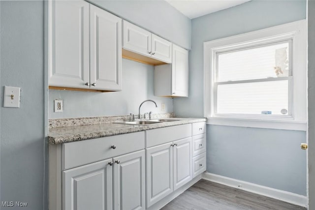 kitchen with white cabinetry, sink, light stone countertops, and light wood-type flooring