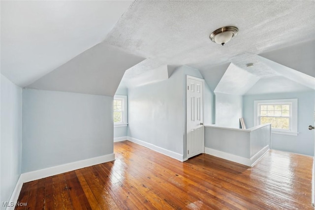 additional living space with wood-type flooring, a textured ceiling, and lofted ceiling