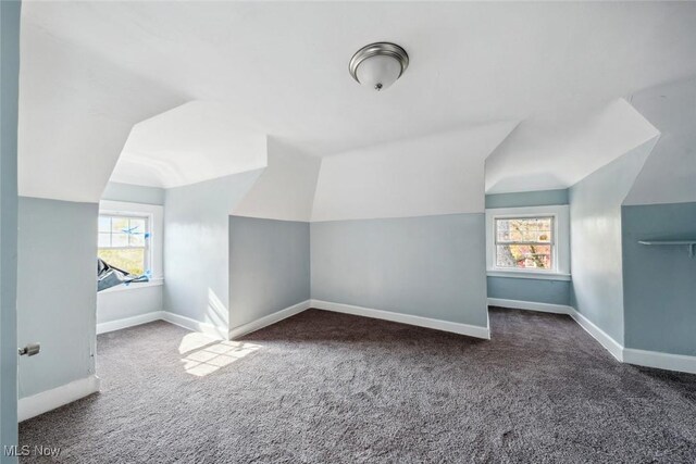 additional living space featuring dark carpet, a healthy amount of sunlight, and vaulted ceiling