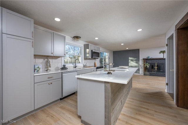 kitchen with sink, a brick fireplace, stainless steel dishwasher, light hardwood / wood-style floors, and a kitchen island