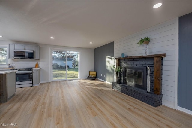 unfurnished living room featuring a brick fireplace, light hardwood / wood-style flooring, and wooden walls