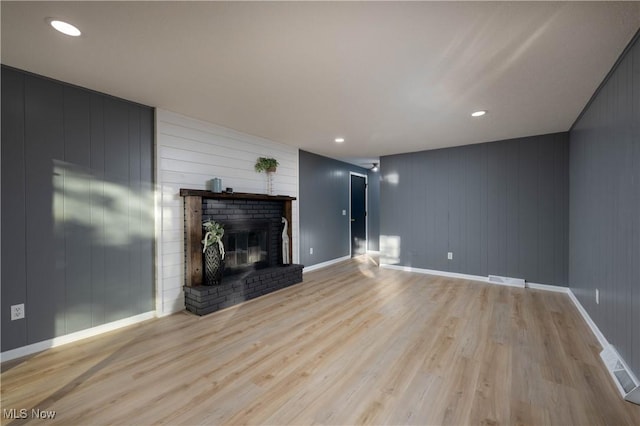 unfurnished living room with wood walls, a fireplace, and light wood-type flooring