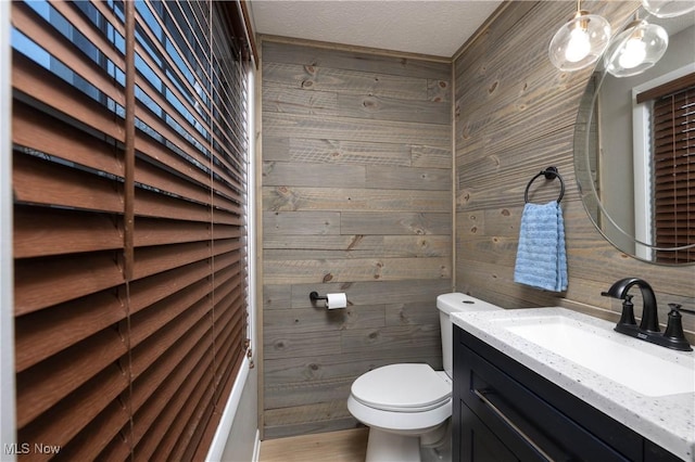 bathroom featuring vanity, wood walls, toilet, and a textured ceiling