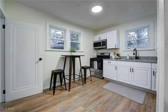 kitchen featuring appliances with stainless steel finishes, white cabinetry, sink, light hardwood / wood-style flooring, and crown molding